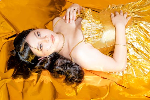 A Woman in Gold Dress Lying on the Floor while Wearing a Gold Necklace