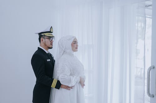 Man in Black Captain Suit Standing Behind Woman in White Wedding Dress