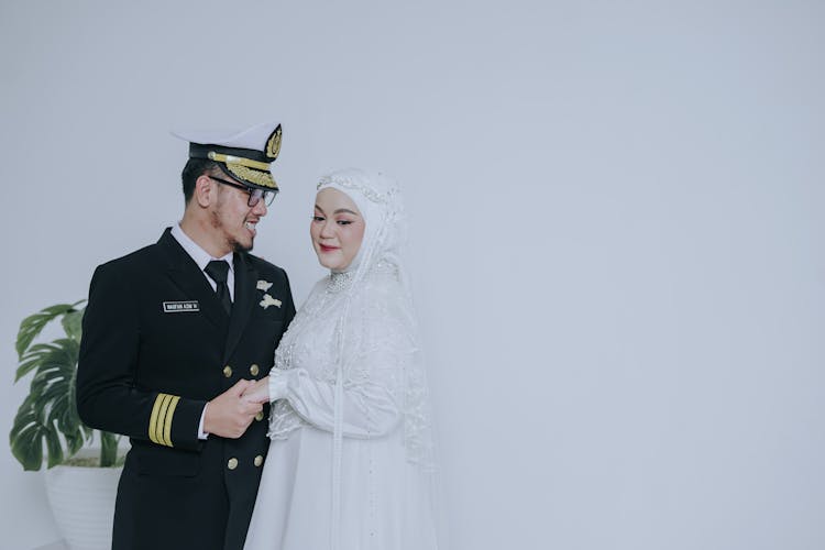 Man In Black Captain Suit Standing Beside Woman In White Wedding Dress