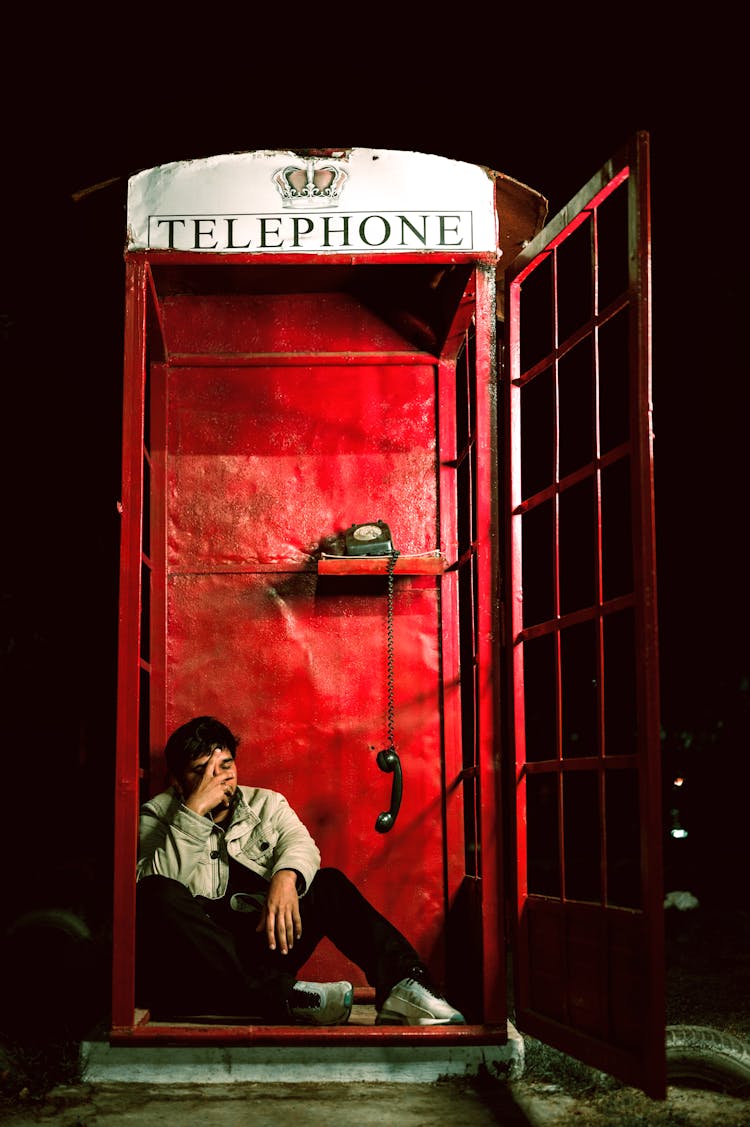 A Man Sitting Inside The Telephone Booth With His Hand On His Face