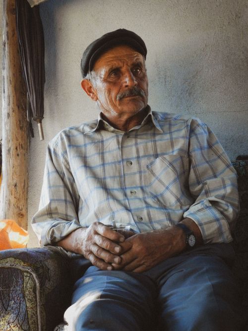 Free Portrait of an elderly man with a mustache sitting on an armchair indoors. Stock Photo