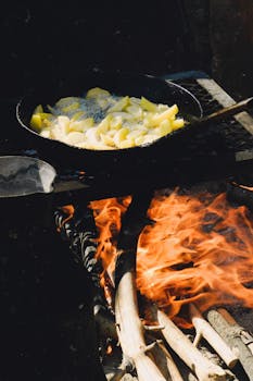 Outdoor frying pan with sizzling potatoes over a rustic open fire.