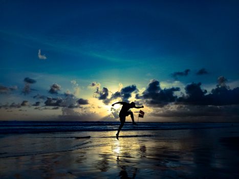 A person jumping on a beach with a dramatic sunset behind them, creating a striking silhouette.