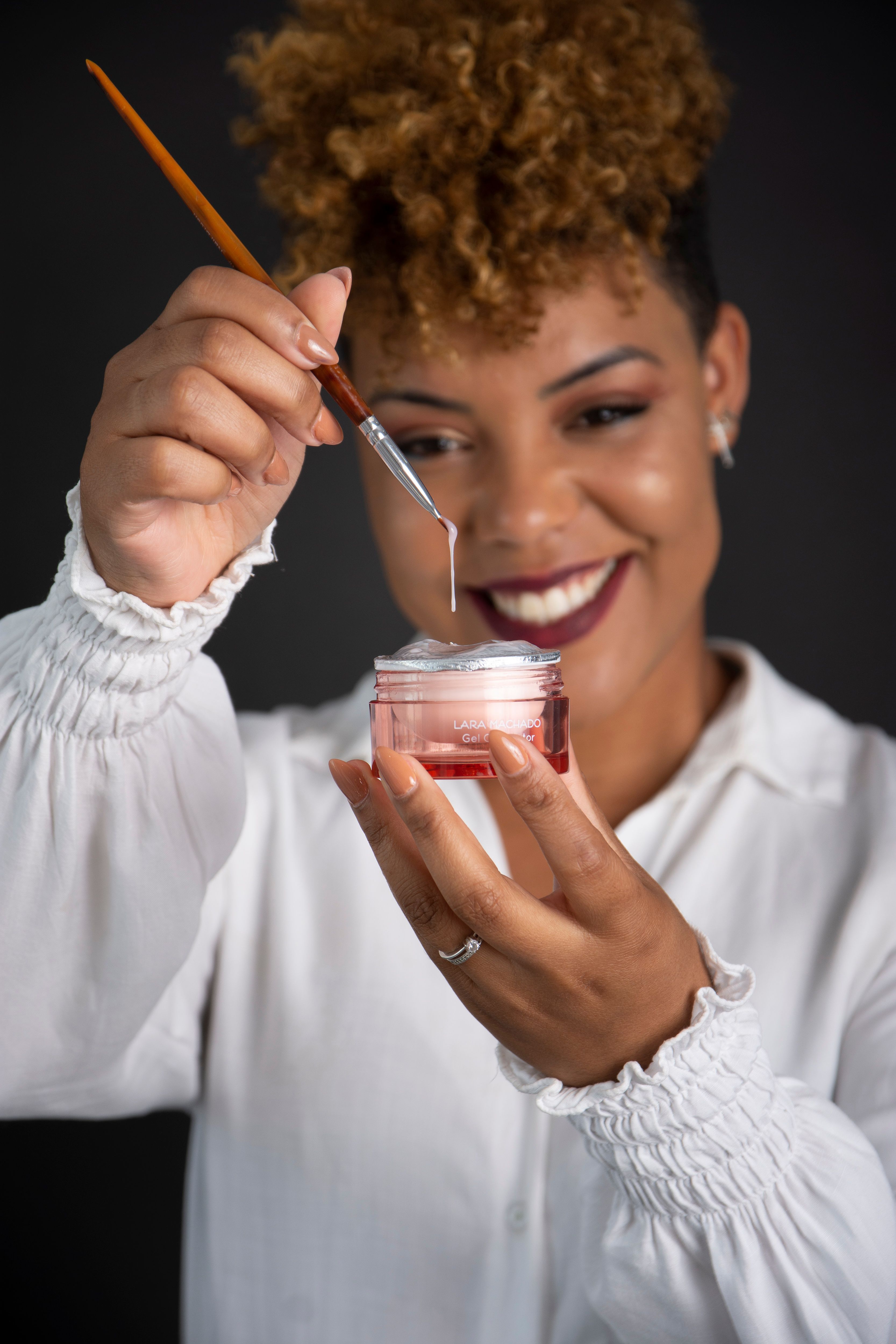 Smiling woman holding a jar of skincare cream with a brush.