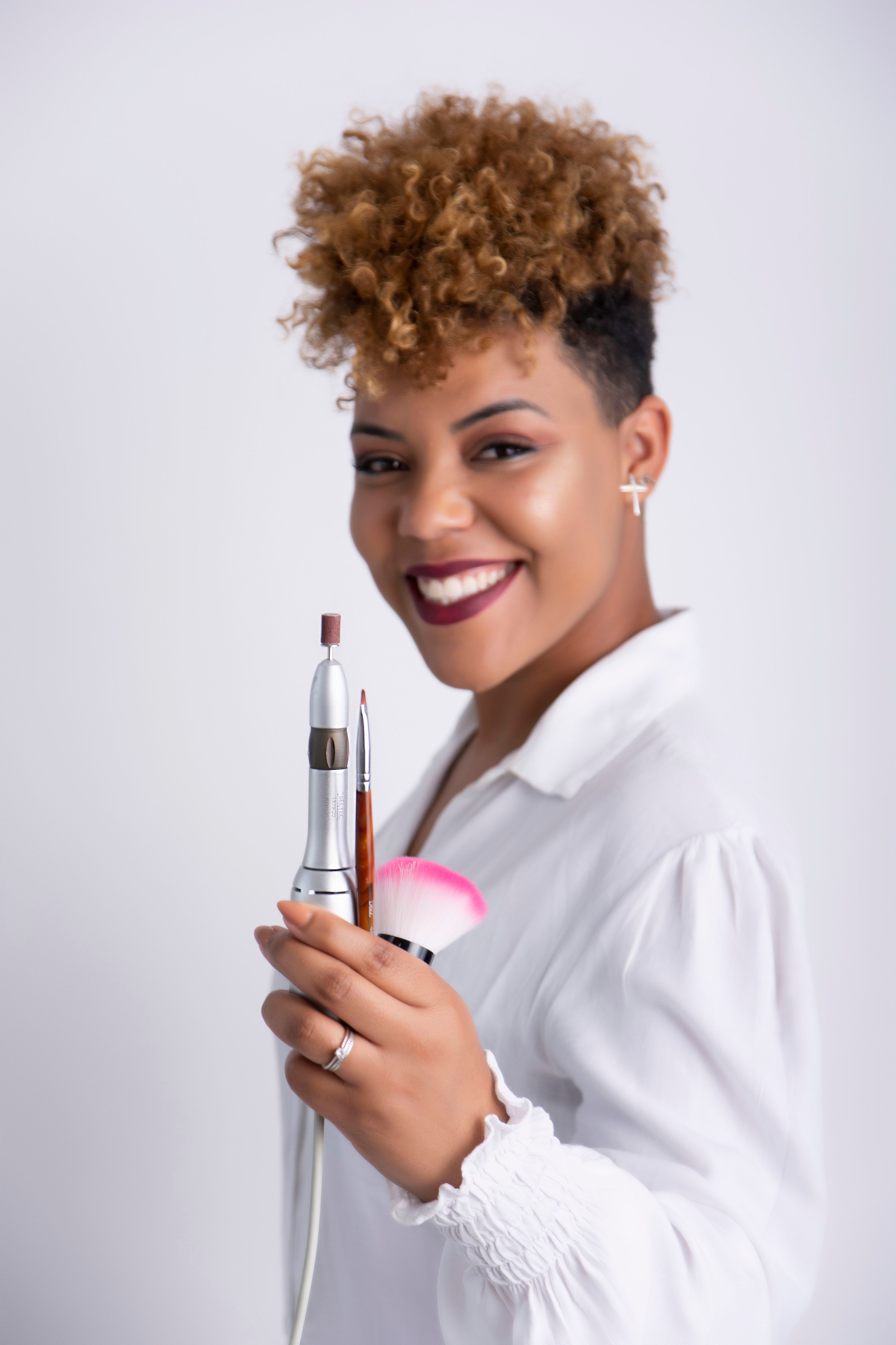 A joyful woman in white holding makeup brushes, showcasing beauty and confidence.