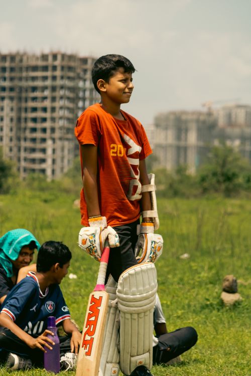 Free Children enjoying a cricket game outdoors near city buildings. Stock Photo