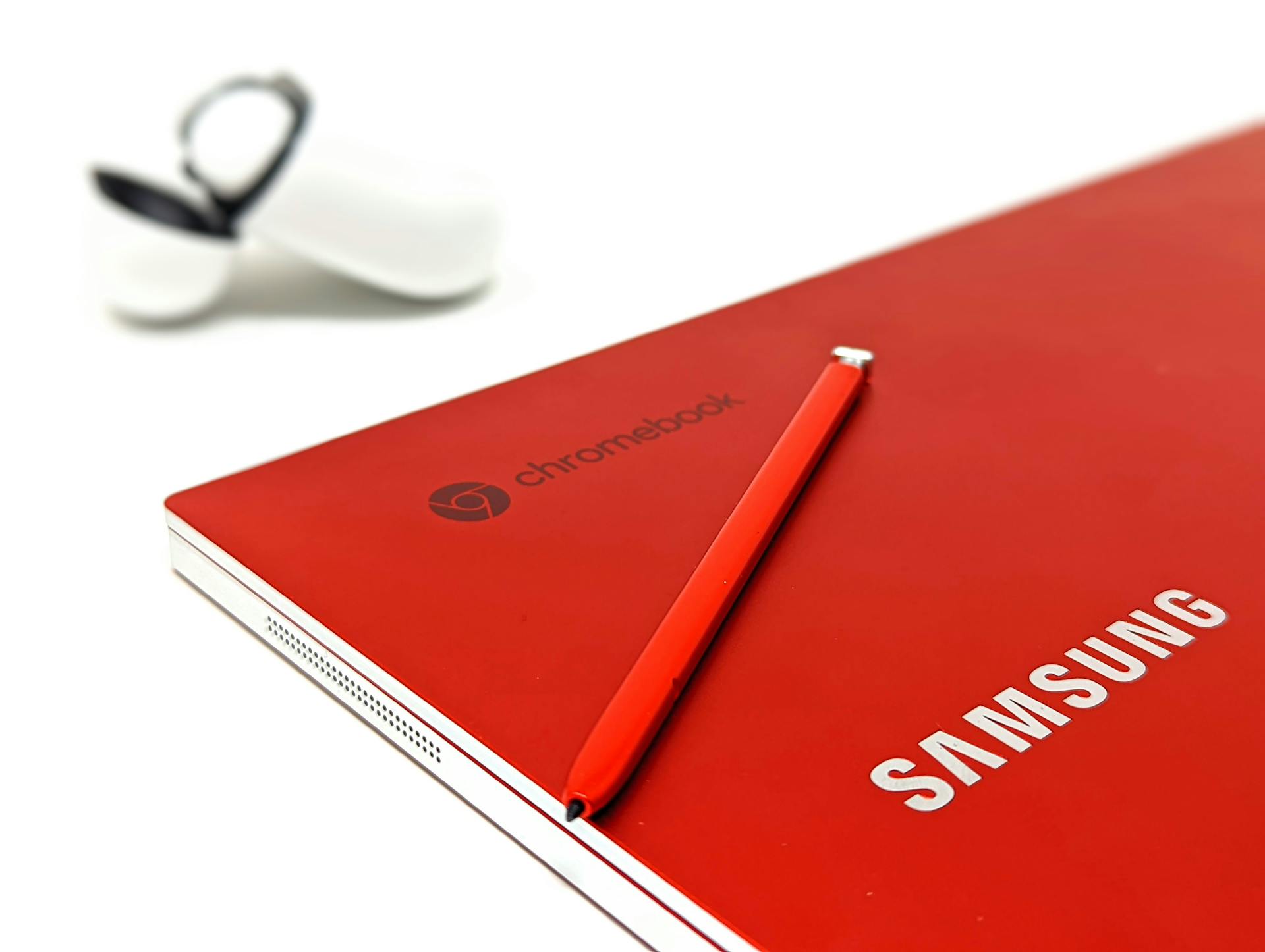 Close-up of a red Samsung Chromebook with stylus and earbuds case, highlighting sleek design.