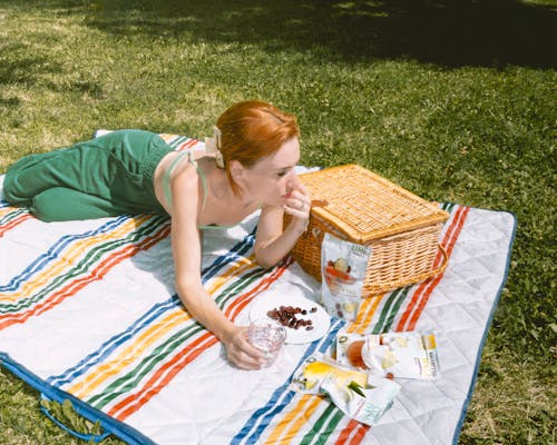 Woman in Green Clothes Lying Down on Picnic Blanket