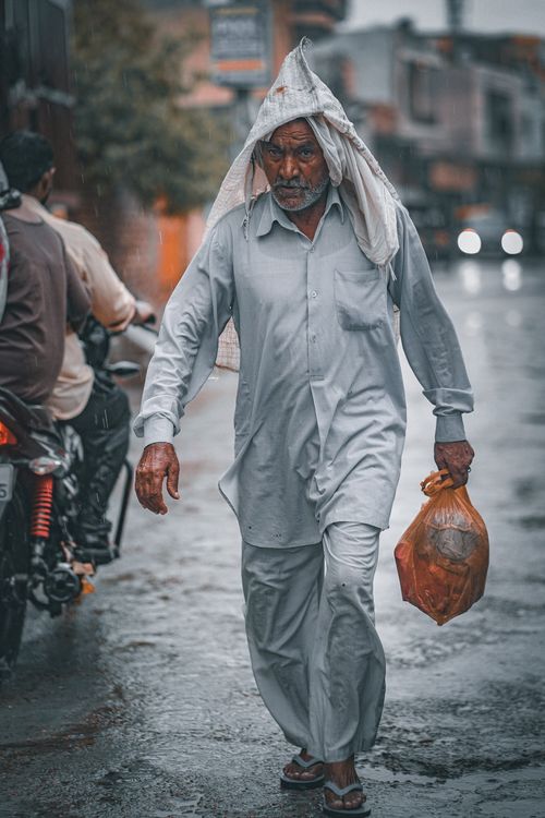 Free Senior man with plastic bag walking on rain-soaked street, covering head with cloth. Stock Photo