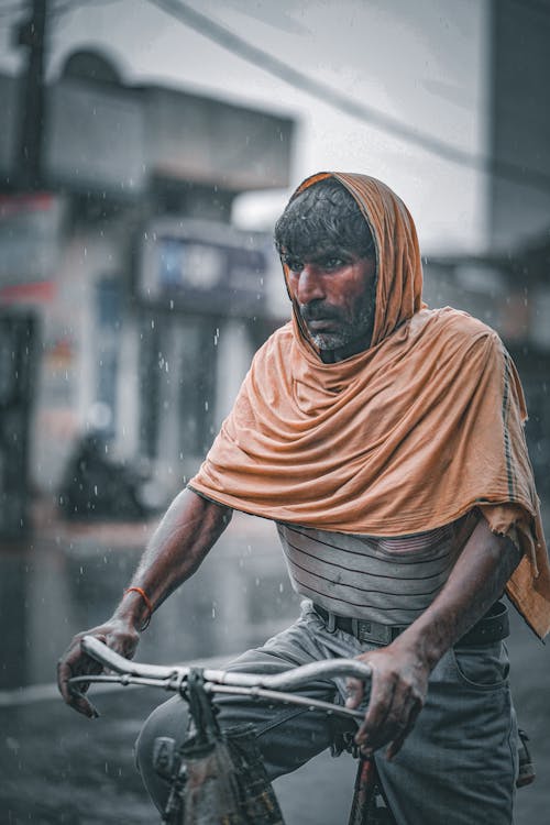 Man Wearing Hijab Riding a Bicycle During Rainy Day