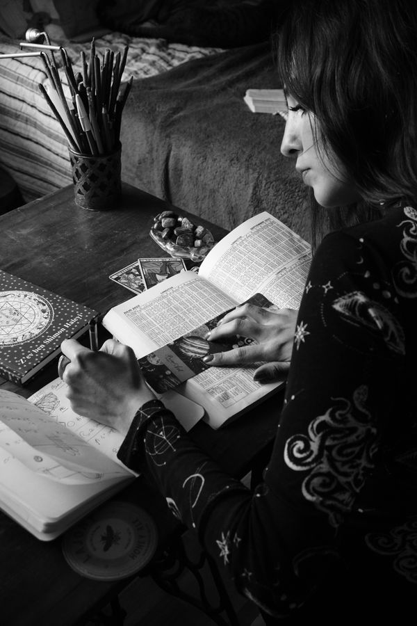 Free Black and white image of a woman writing about astrology in a notebook, surrounded by related items. Stock Photo