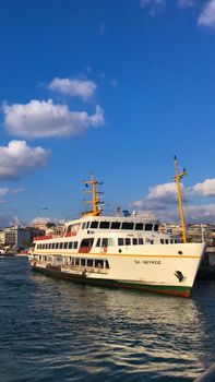 A ferry docked at an Istanbul port under a vibrant blue sky with scattered clouds.