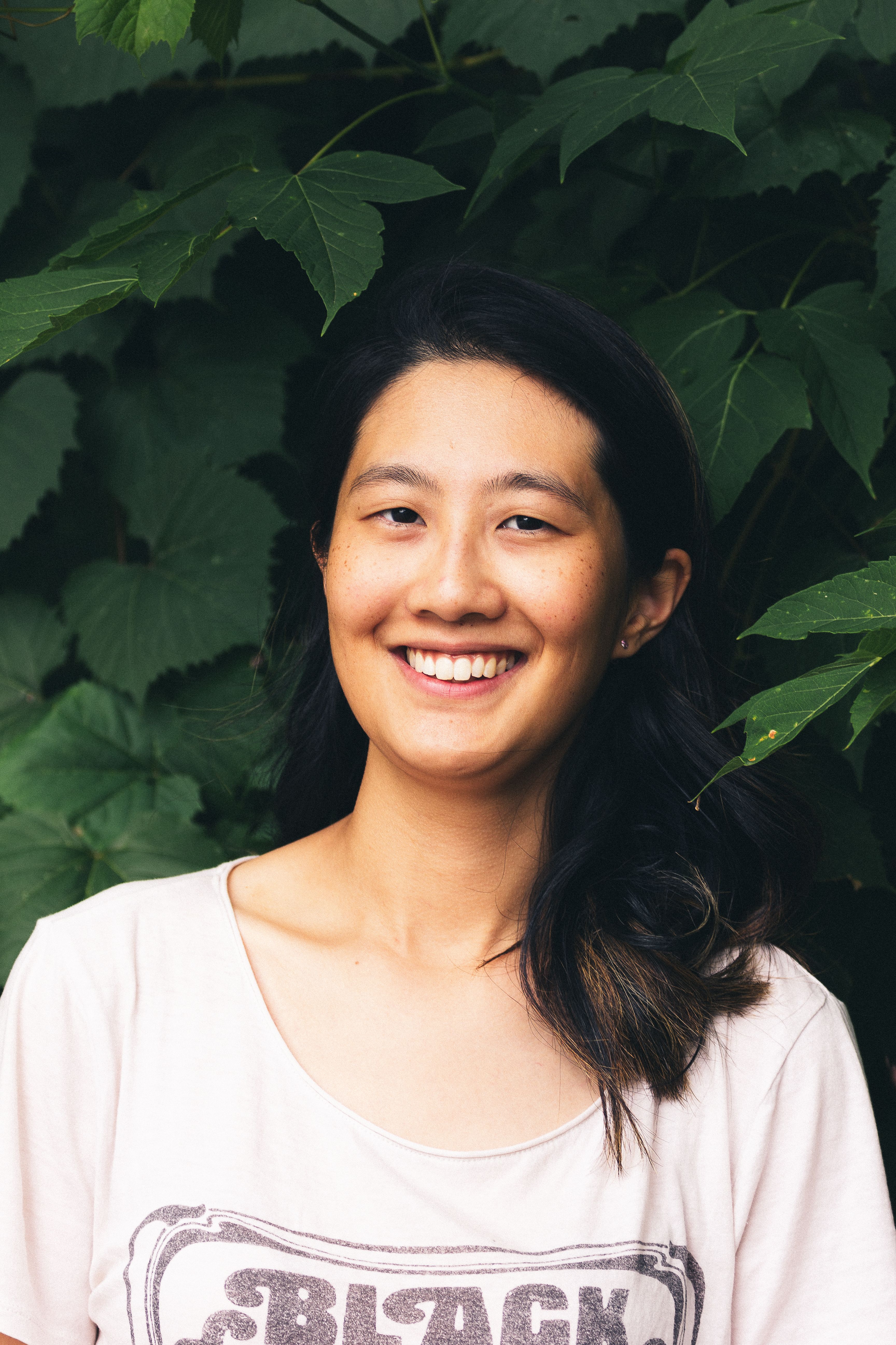 Cheerful young woman smiling outdoors, surrounded by lush greenery.