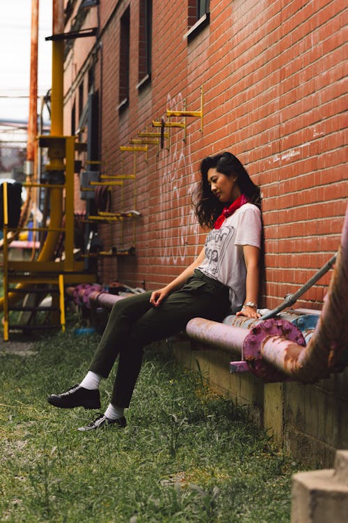 A Woman in White Shirt Sitting Near the Brick Wall with Her Legs Crossed