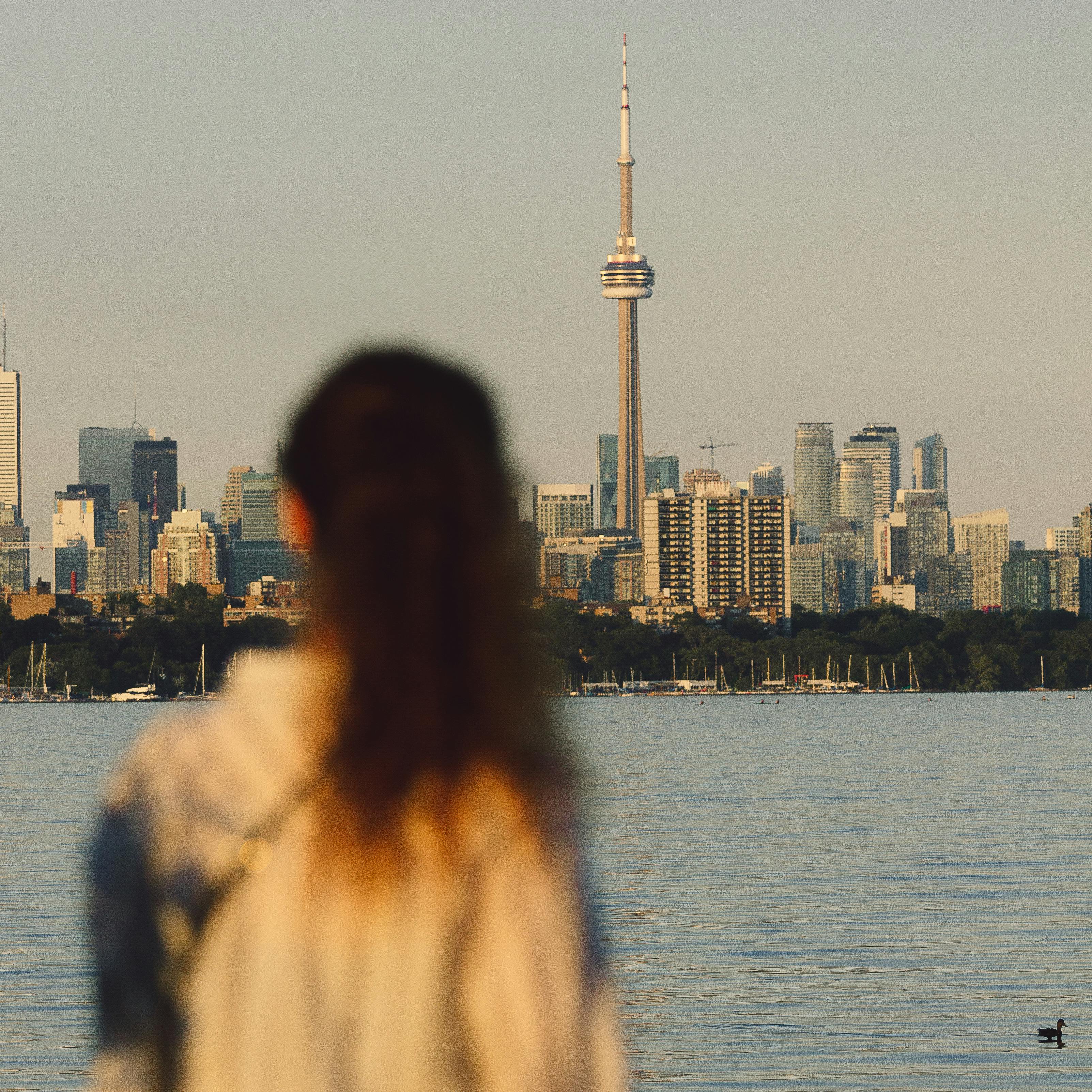 A woman gazes across the water at the Toronto skyline featuring the CN Tower.