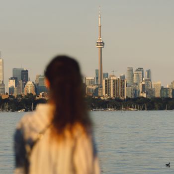 A woman gazes across the water at the Toronto skyline featuring the CN Tower.