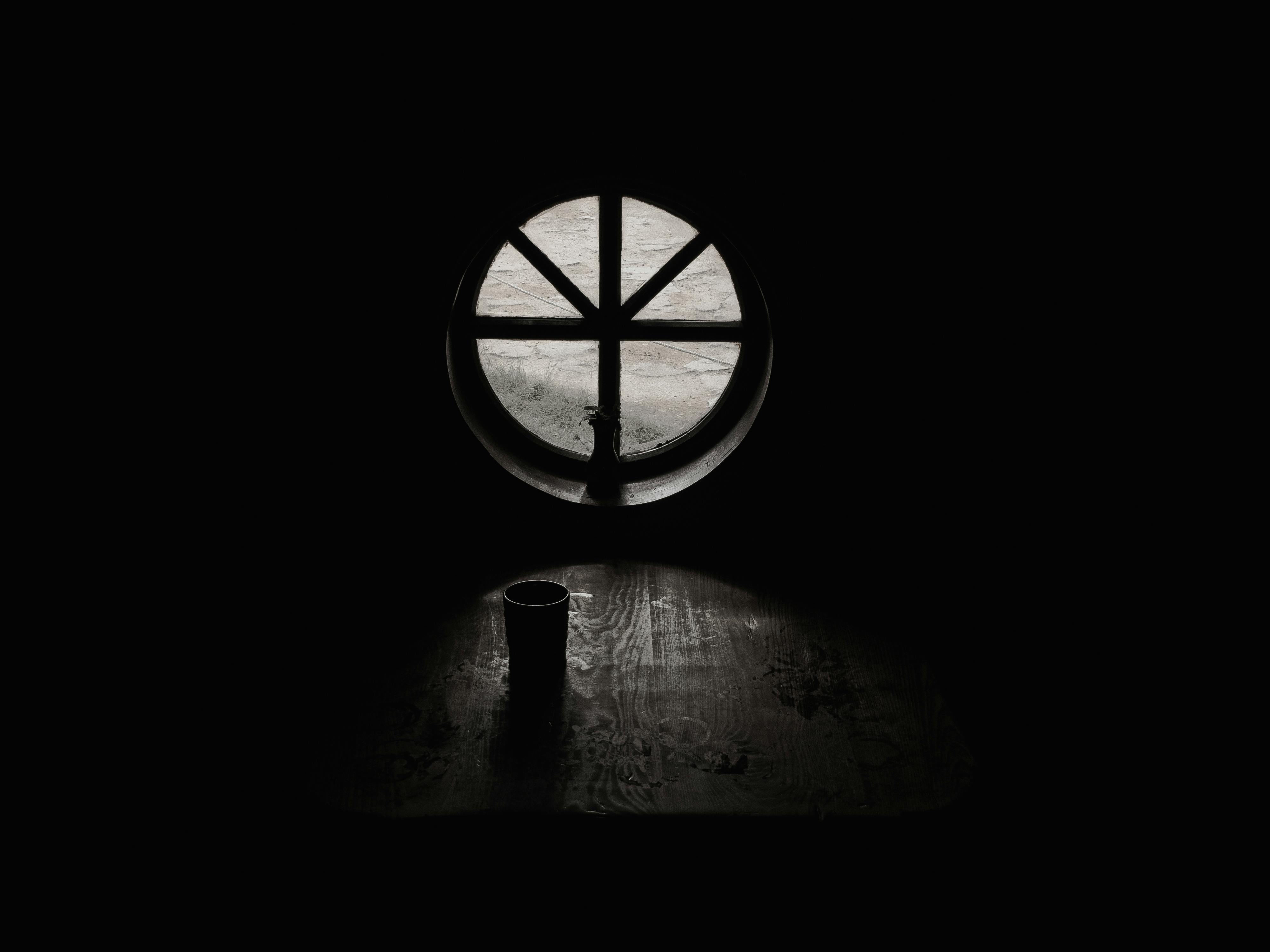 grayscale photography of cup beside closed window in empty room