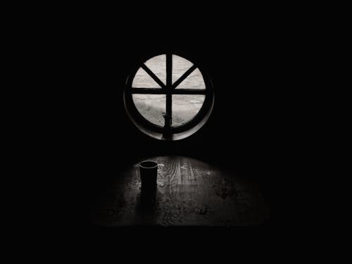 空房间里关闭的窗户旁边的杯子的灰度摄影
