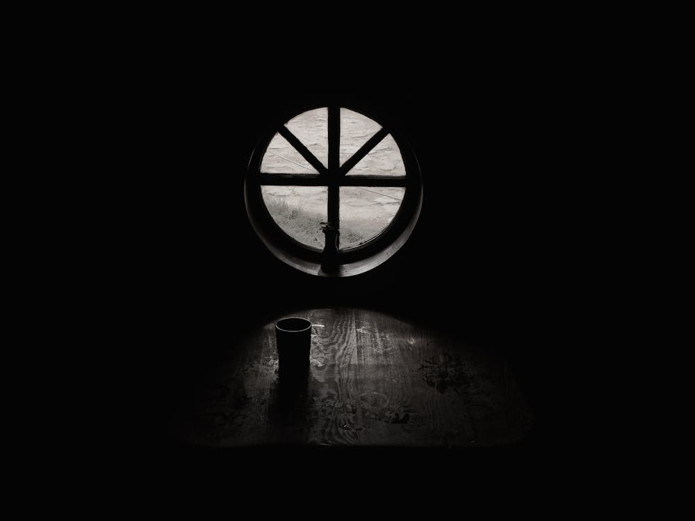 空房間里關閉的窗戶旁邊的杯子的灰度攝影