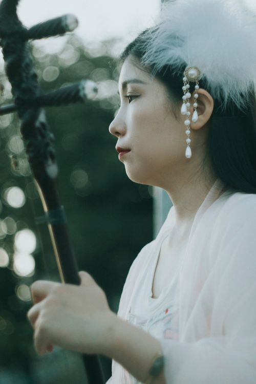 Free Profile of an Asian woman in white attire playing a traditional string instrument outdoors. Stock Photo