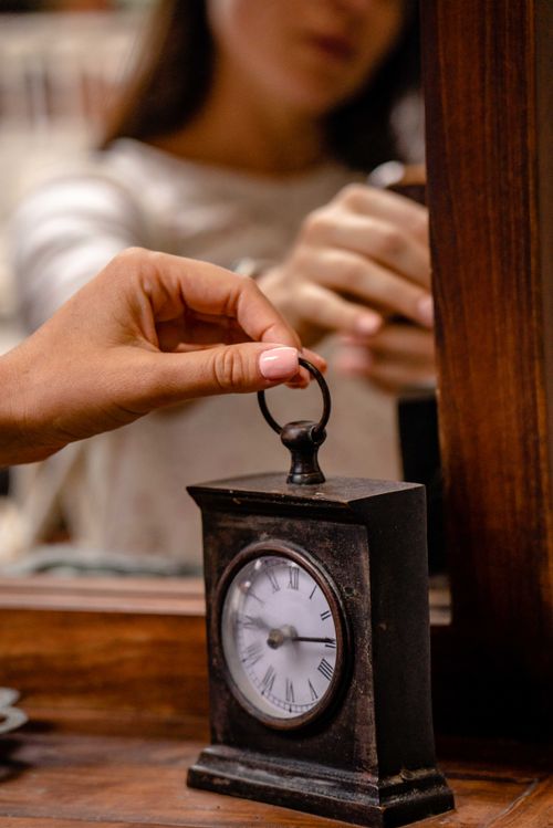 Free A woman holds a vintage clock in front of a mirror, reflecting her hand and the clock. Stock Photo