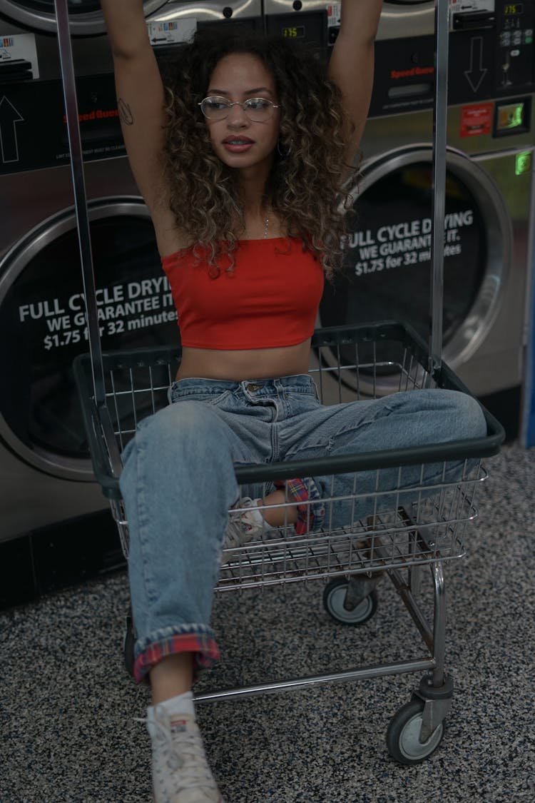 A Woman In Red Tube Top And Denim Jeans Sitting On A Stainless Cart