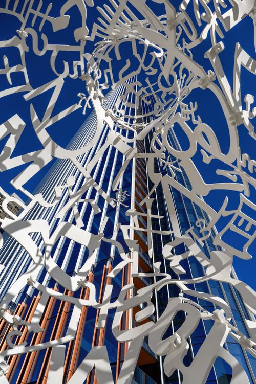 Free An abstract sculpture of letters frames a modern skyscraper against a clear blue sky. Stock Photo
