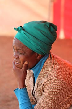 一位穿着图案外套、头戴绿色头巾的老妇人陷入了沉思