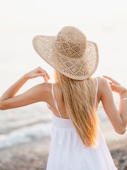 A woman in a sun hat and white dress enjoys the seaside view, exuding summer vibes.
