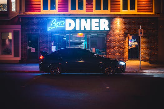 A sleek black sports car parked in front of Pop's Diner with vibrant neon lights at night.