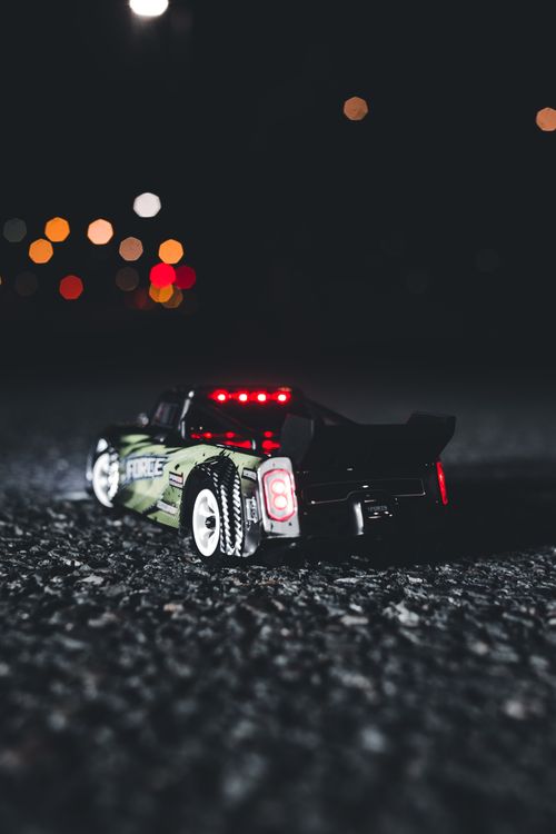 Free Close-up of a toy car with colorful bokeh lights in the background at nighttime on asphalt. Stock Photo