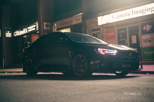 Free A sleek black sports car parked at night on a city street with illuminated store signs. Stock Photo