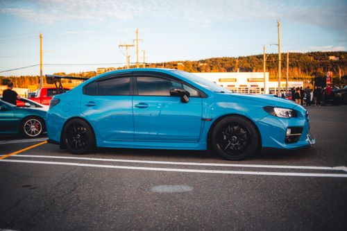 Free A striking blue Subaru WRX STI sports car parked in a lot during a scenic sunset, showcasing automotive elegance. Stock Photo