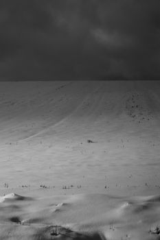 Dramatic snowy landscape under dark clouds in Sweden, capturing winter's stark beauty.