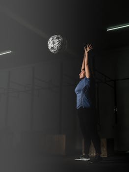 A woman in active wear stretching indoors while lifting a medicine ball.