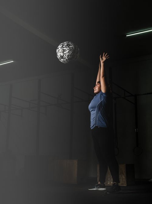 Free A woman in active wear stretching indoors while lifting a medicine ball. Stock Photo
