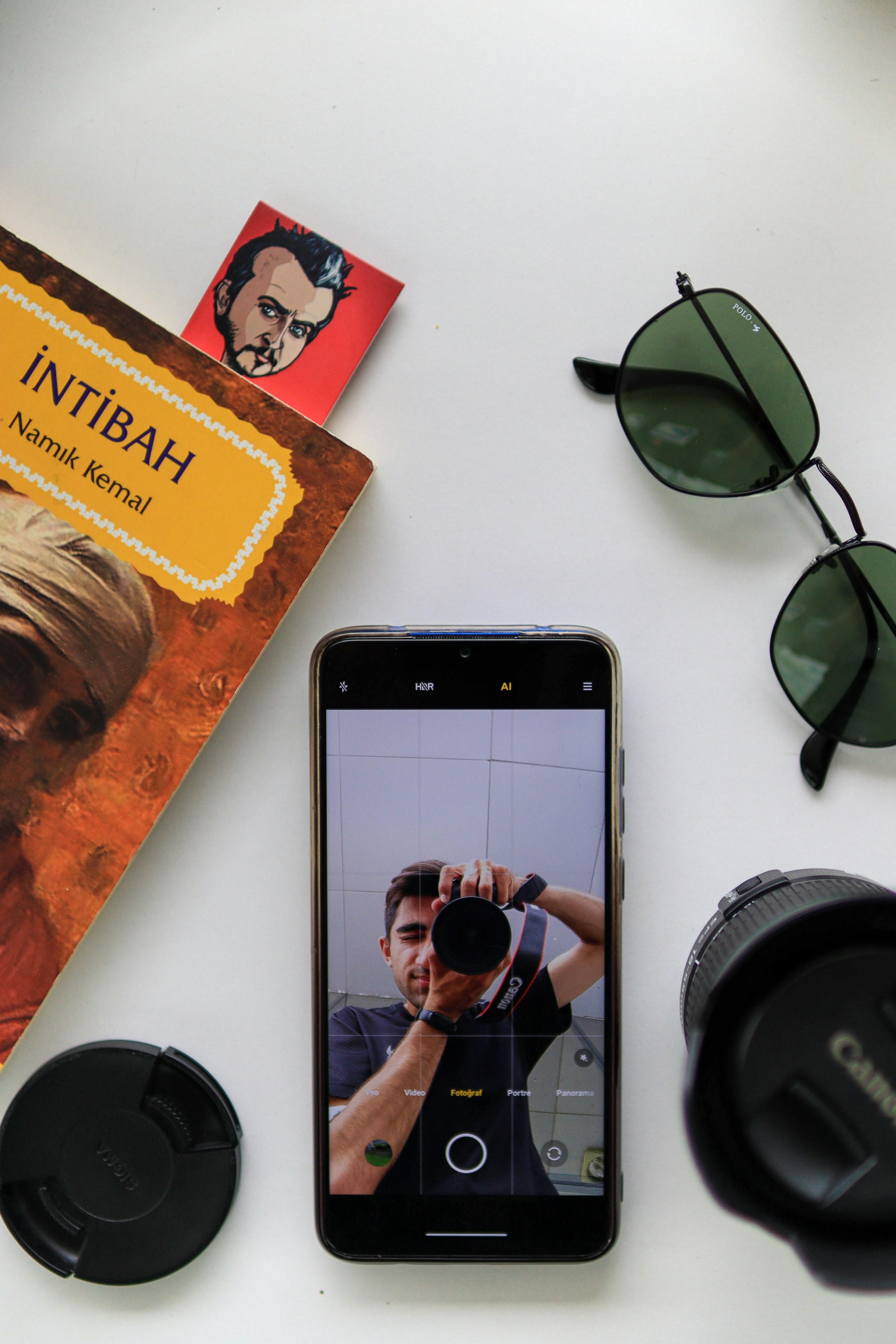 Free Flat lay of a smartphone displaying a photo, surrounded by sunglasses and a book. Stock Photo