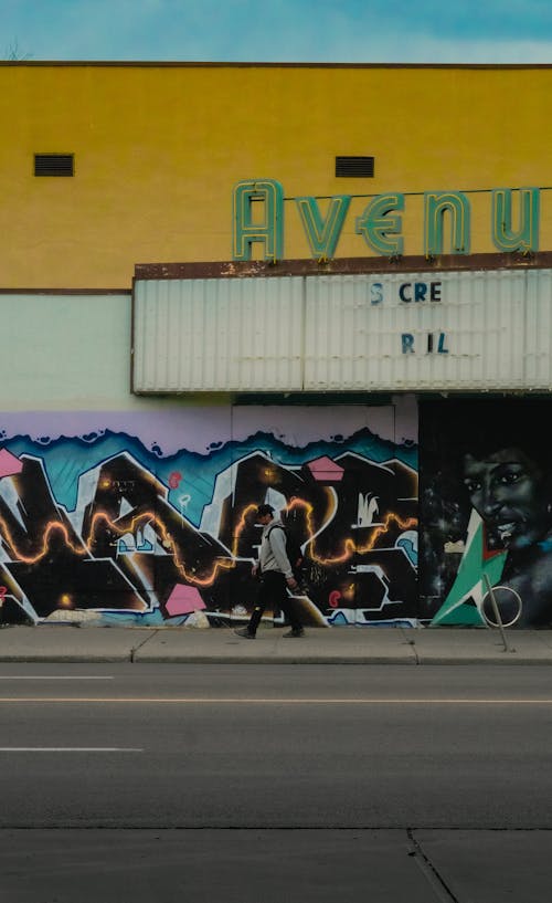 A Person Walking on the Street Near the Building with Graffiti