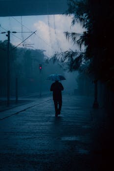 A lone person walks under an umbrella through rain-soaked streets in Kolkata, India.