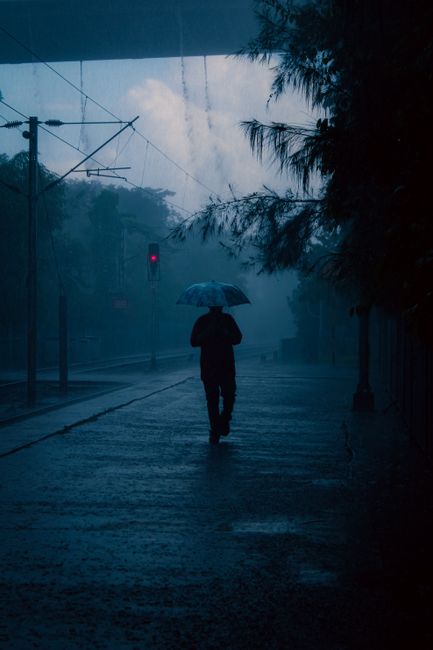 A lone person walks under an umbrella through rain-soaked streets in Kolkata, India.