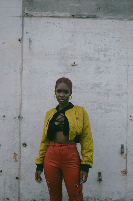 Stylish portrait of a woman in urban Accra, Ghana against a concrete wall. Vibrant outfit in yellow and red.