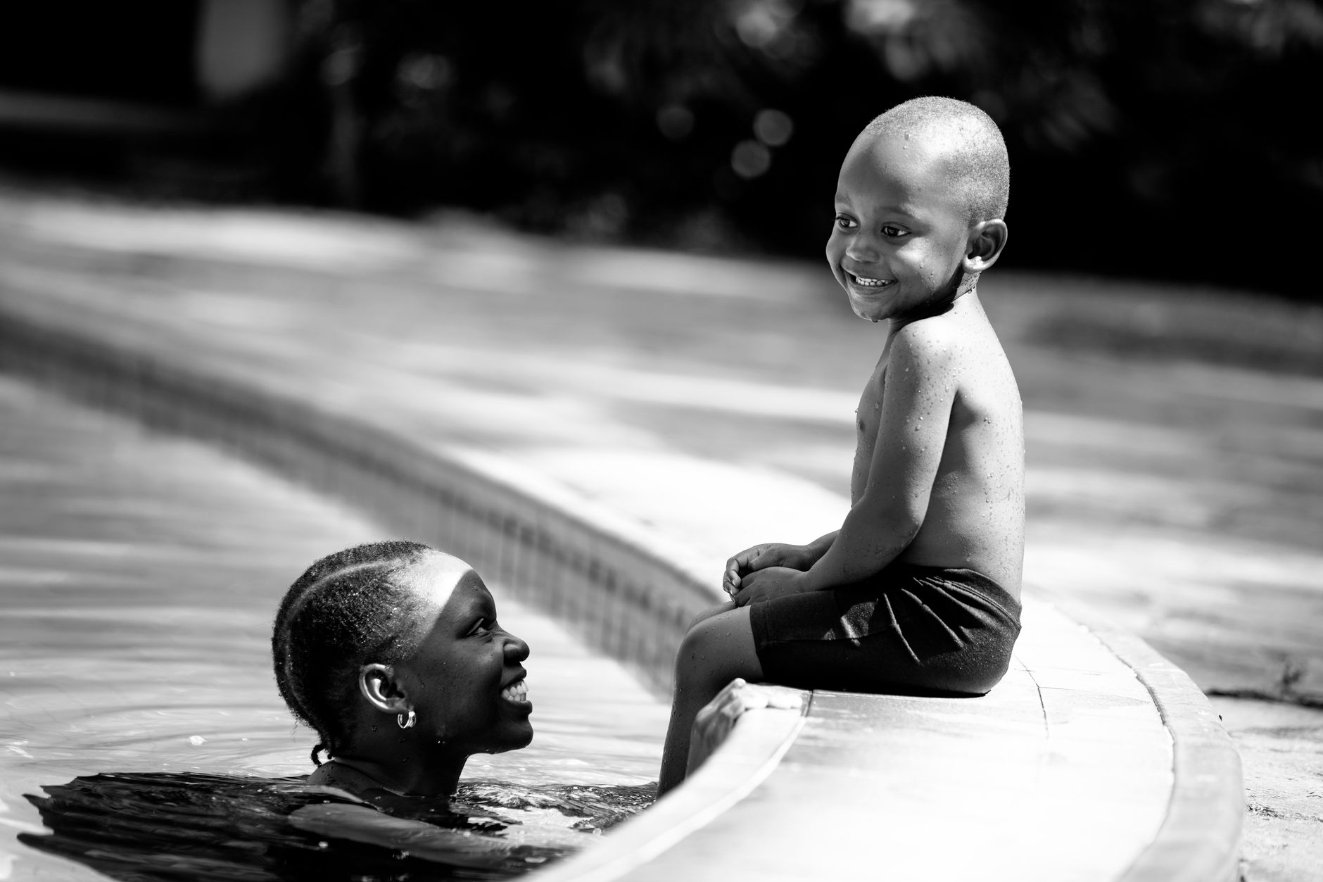 A joyful black and white photo of a mother and son by the swimming pool on a sunny day.