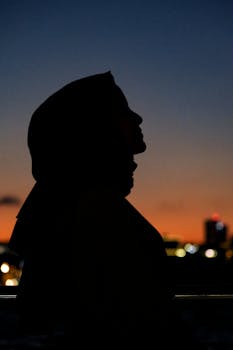 A woman's silhouette at twilight with a vibrant skyline in the background.