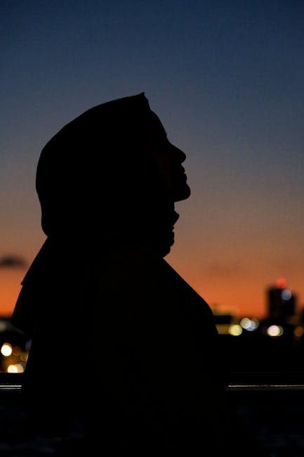 A woman's silhouette at twilight with a vibrant skyline in the background.