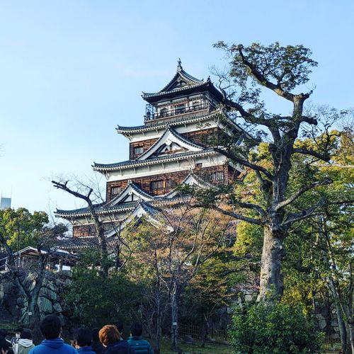 Free Capturing the grand architecture of Hiroshima Castle amidst lush trees under a clear sky. Stock Photo