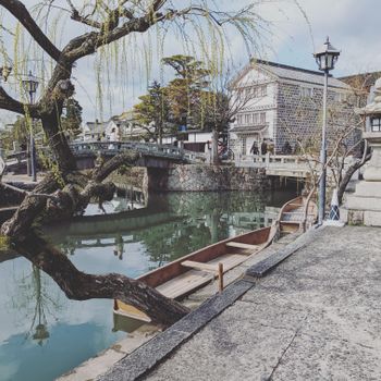 A serene canal view featuring a traditional wooden boat, arched bridge, and historic architecture.（イメージ）