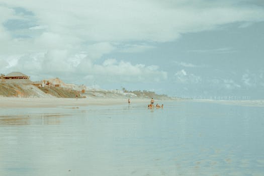 A tranquil Brazilian beach scene with people enjoying summer. Wind turbines visible in the distance.