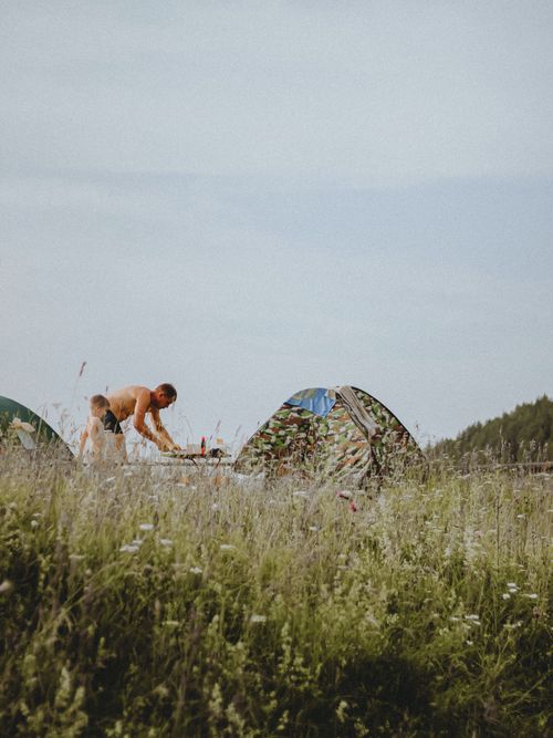 Free A man and boy enjoy a camping experience by their tent in a grassy field. Stock Photo