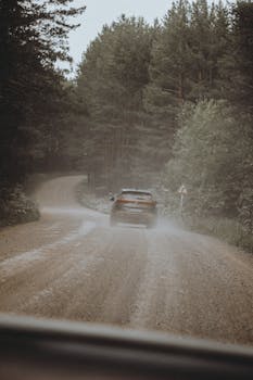 A car navigates a dusty, unpaved road through a lush green forest area.