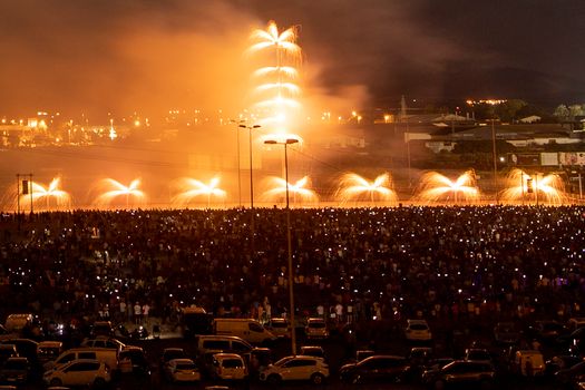 Dazzling fireworks light the night sky above a large audience in a cityscape setting.